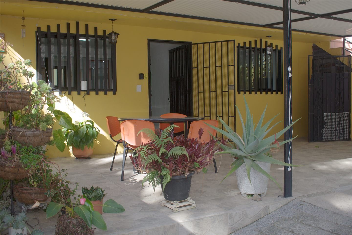 Terraza cubierta de El Refugio, con mesa, materas y la puerta abierta, rodeada de verde